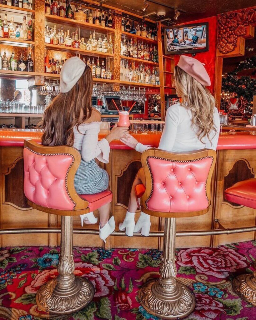 2 friends toasting pink milkshakes at the ornate, pink-accented bar of the Madonna Inn's Cafe. Photo by @trippingwithmybff