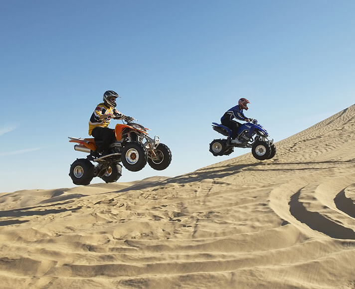 Two ATV riders soaring through the Oceano Dunes