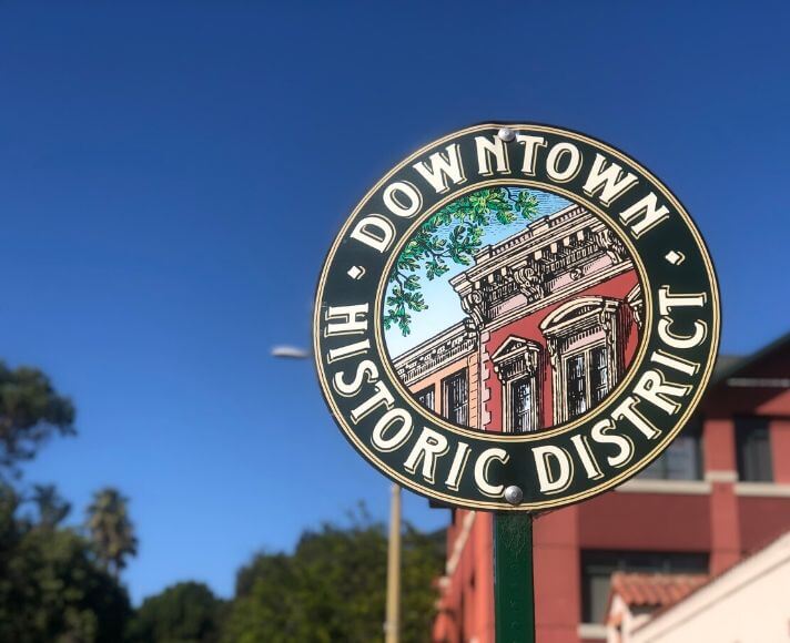 The round Downtown Historic District street sign in front of a brick building and blue sky in San Luis Obispo, California.